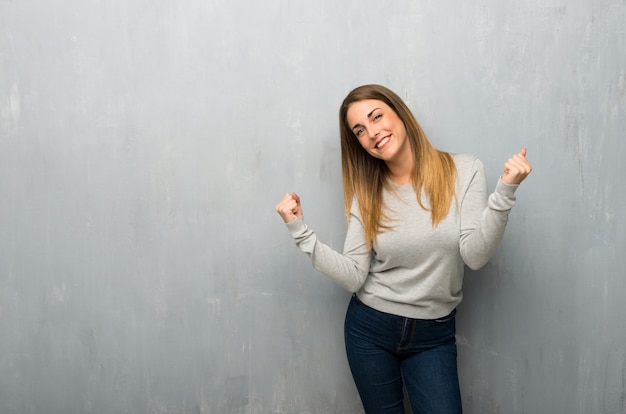 Mujer joven en la pared con textura celebrando una victoria