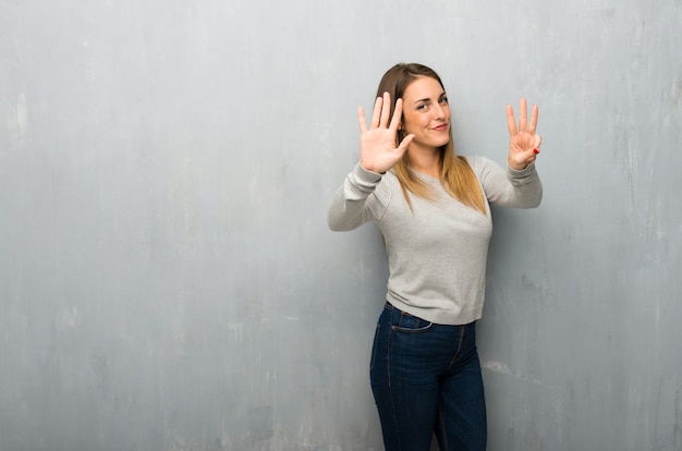 Mujer joven en la pared con textura contando ocho con los dedos