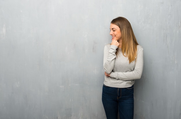 Mujer joven en la pared con textura mirando hacia el lado con la mano en la barbilla