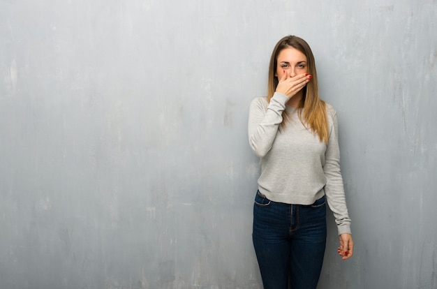 Mujer joven en la pared con textura que cubre la boca con las manos por decir algo inapropiado