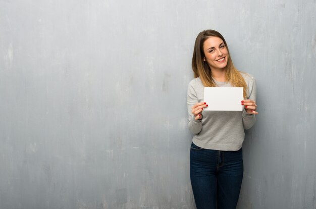 Mujer joven en la pared con textura que sostiene un cartel para insertar un concepto