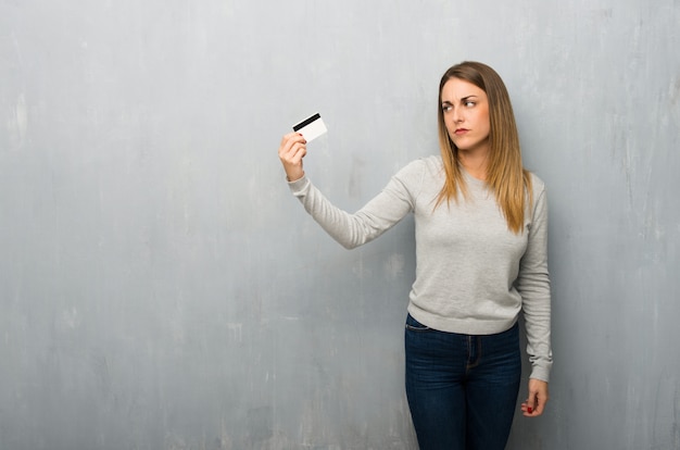 Mujer joven en la pared con textura tomando una tarjeta de crédito sin dinero