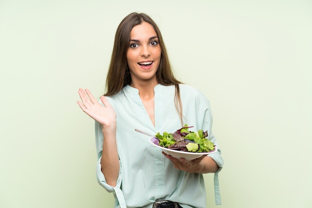 Mujer joven con la pared verde aislada ensalada con la expresión facial de la sorpresa