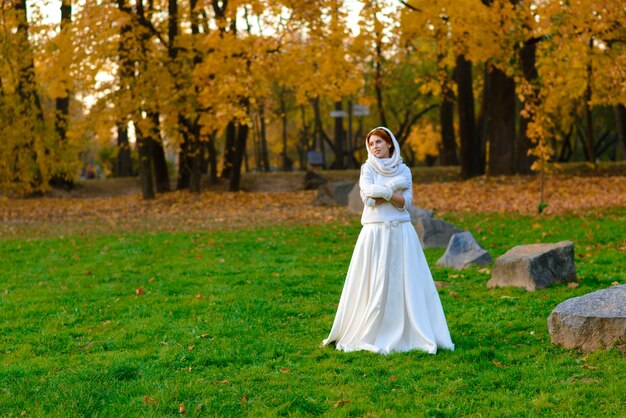 Mujer joven en un parque de otoño. Dama con hojas en vestido blanco