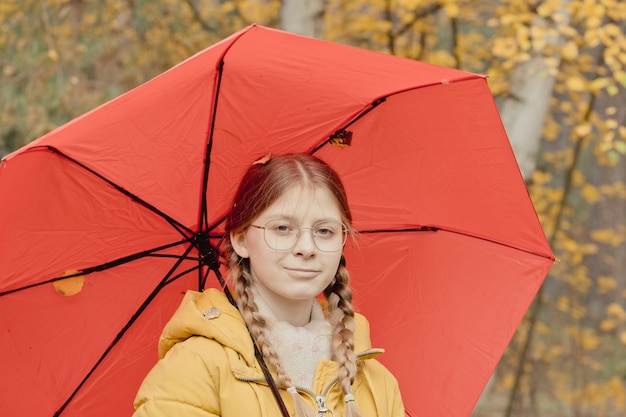 Mujer joven en un parque de otoño con un paraguas rojo, girando y sosteniendo un paraguas, paseo de otoño en un parque de octubre amarillo