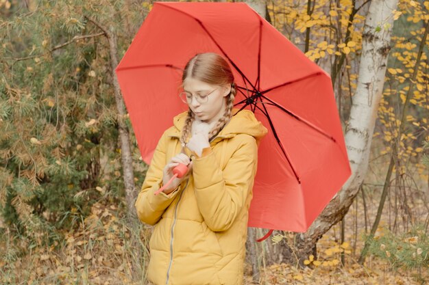 Mujer joven en un parque de otoño con un paraguas rojo, girando y sosteniendo un paraguas, paseo de otoño en un parque de octubre amarillo