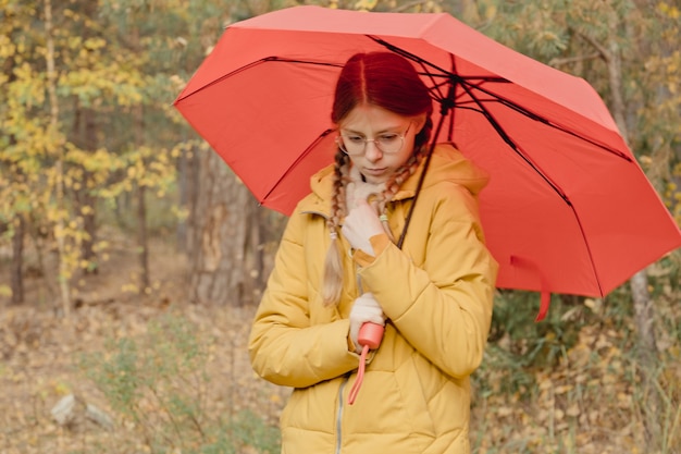 Mujer joven en un parque de otoño con un paraguas rojo, girando y sosteniendo un paraguas, paseo de otoño en un parque de octubre amarillo