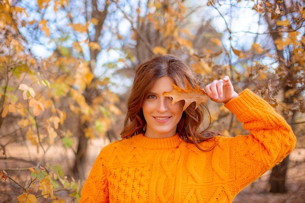 Una mujer joven en un parque de otoño con un suéter naranja