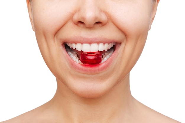 Mujer joven con pastillas rojas para el dolor de garganta en los dientes. chupando caramelo en la boca