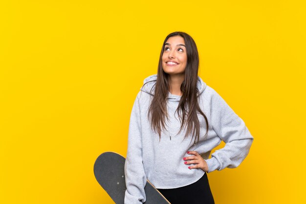 Mujer joven del patinador aislada en el amarillo que mira para arriba mientras que sonríe