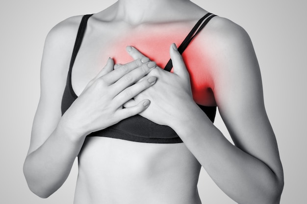 Mujer joven con pecho, dolor de corazón sobre fondo gris. Fotografía en blanco y negro con punto rojo.