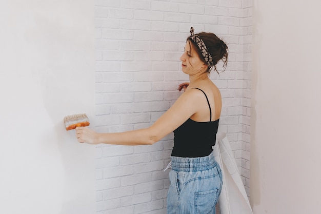 Mujer joven pega papel tapiz en casa. chica pega papel tapiz en forma de ladrillo. reparar.