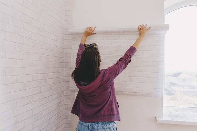 Mujer joven pega papel tapiz en casa. chica pega papel tapiz en forma de ladrillo. reparar.