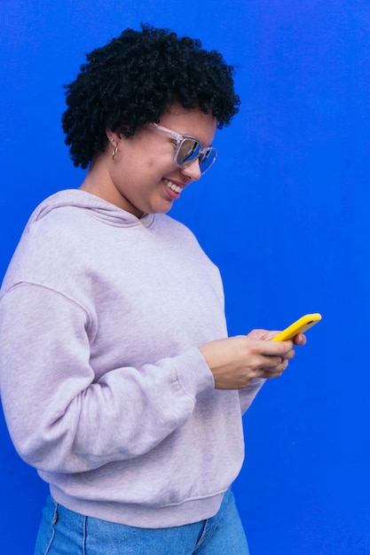 Mujer joven peinado afro con gafas enviando mensajes de texto con su teléfono inteligente