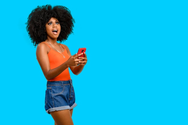 Mujer joven con peinado afro sosteniendo teléfono celular aislado sobre fondo gris, concepto de publicidad de persona.