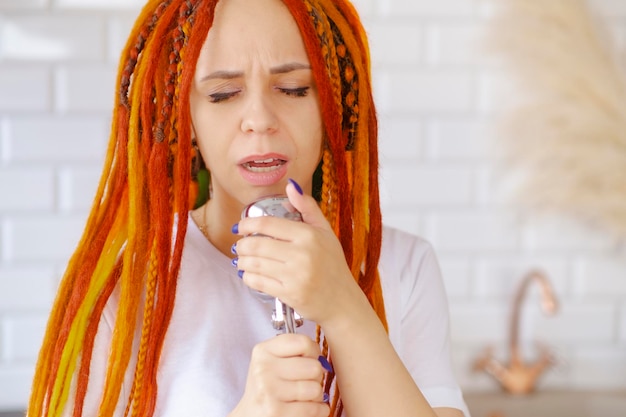 Mujer joven con peinado brillante con micrófono retro en la cocina Retrato de cantante femenina con rastas cantando en el micrófono en casa