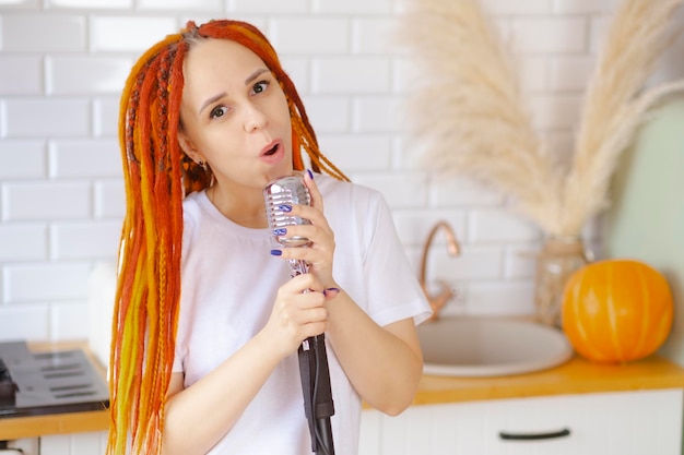 Mujer joven con peinado brillante con micrófono retro en la cocina Retrato de cantante femenina con rastas cantando en el micrófono en casa