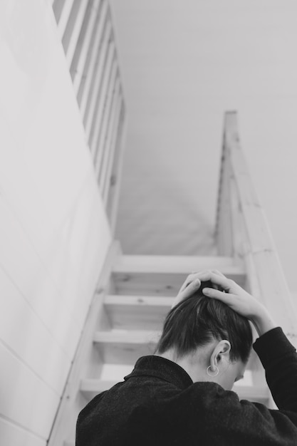 Foto mujer joven peinado simple vista posterior por escaleras de madera en casa depresión soledad y concepto de cuarentena salud mental autocuidado quedarse en casa