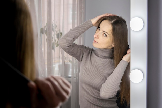 Mujer joven peinándose mientras se mira en el espejo