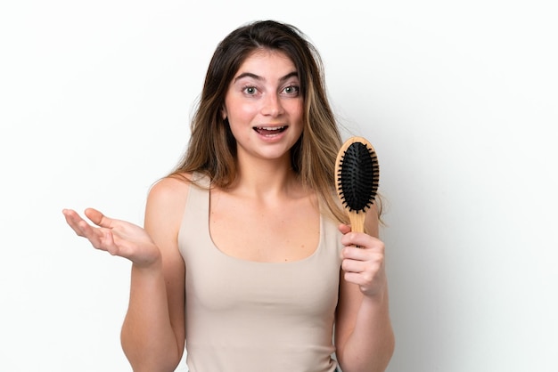 Mujer joven con peine de cabello aislado en fondo blanco con expresión facial conmocionada