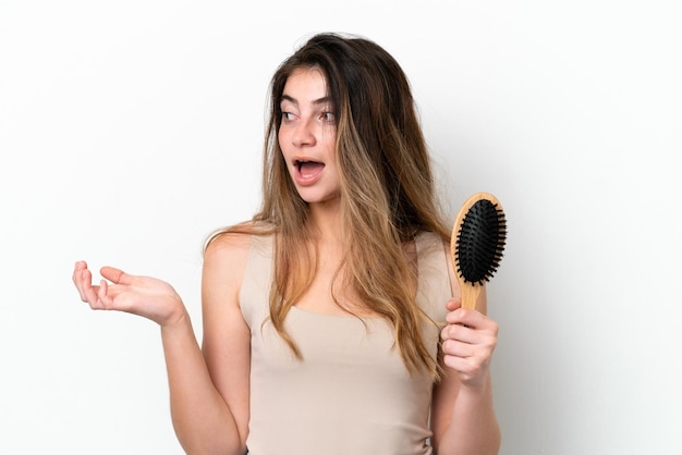 Mujer joven con peine de cabello aislado en fondo blanco con expresión facial de sorpresa