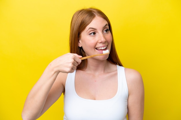 Mujer joven pelirroja aislada sobre fondo amarillo con un cepillo de dientes