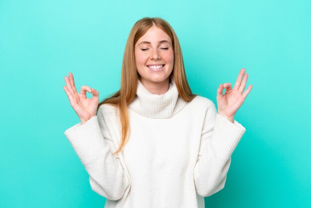 Mujer joven pelirroja aislada sobre fondo azul en pose zen