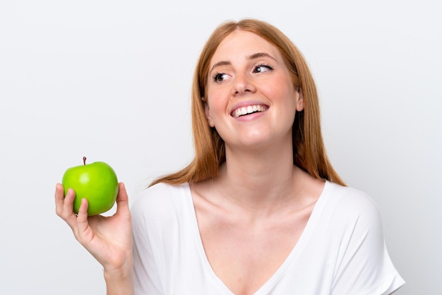 Mujer joven pelirroja aislada sobre fondo blanco con una manzana y feliz