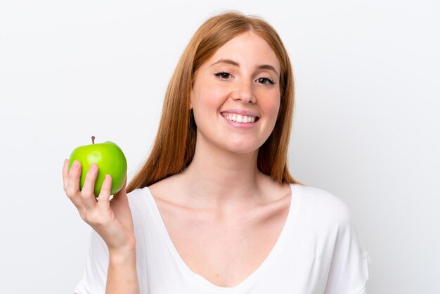 Mujer joven pelirroja aislada sobre fondo blanco con una manzana y feliz