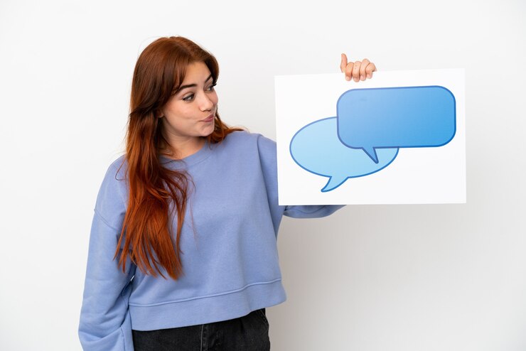 Foto mujer joven pelirroja aislada sobre fondo blanco sosteniendo un cartel con el icono de la burbuja del discurso