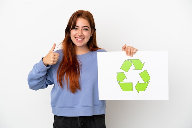 Mujer joven pelirroja aislada sobre fondo blanco sosteniendo un cartel con el icono de reciclaje con el pulgar hacia arriba