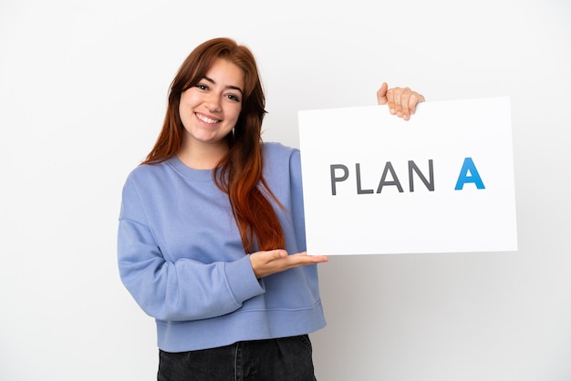 Mujer joven pelirroja aislada sobre fondo blanco sosteniendo un cartel con el mensaje PLAN A con expresión feliz