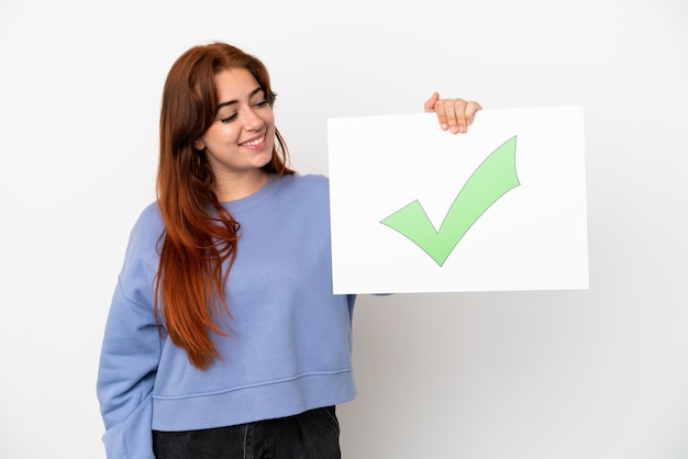 Foto mujer joven pelirroja aislada sobre fondo blanco sosteniendo un cartel con texto icono de marca de verificación verde con expresión feliz