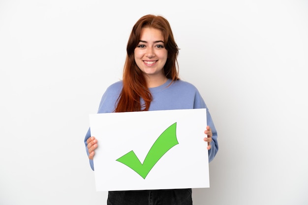 Foto mujer joven pelirroja aislada sobre fondo blanco sosteniendo un cartel con texto icono de marca de verificación verde con expresión feliz