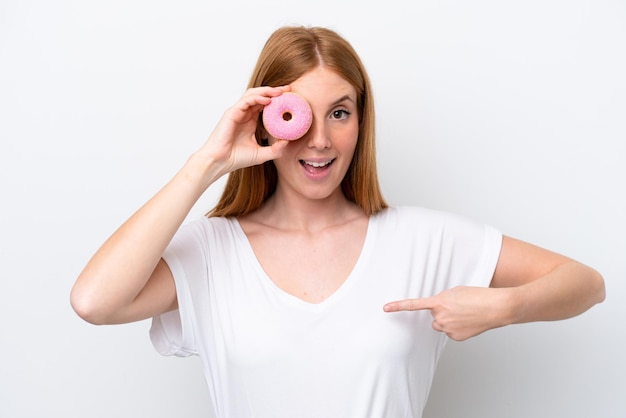 Mujer joven pelirroja aislada sobre fondo blanco sosteniendo un donut y feliz