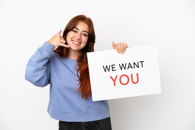 Mujer joven pelirroja aislada sobre fondo blanco sosteniendo We Want You board y haciendo gesto de teléfono