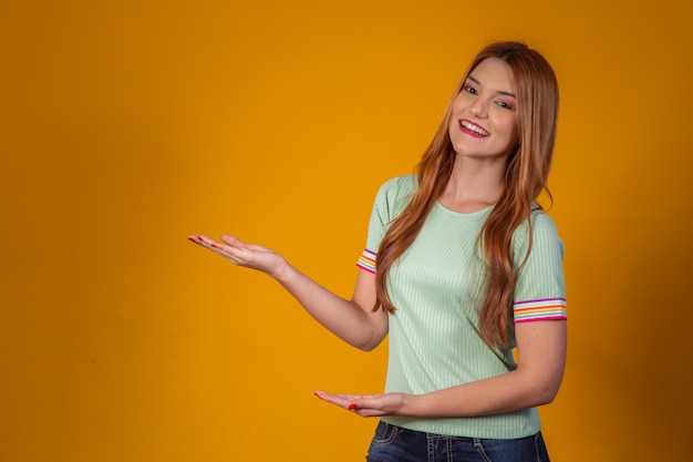 Mujer joven pelirroja apuntando a espacio libre para texto sobre fondo amarillo.