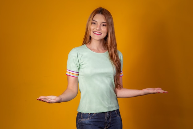 Mujer joven pelirroja apuntando a espacio libre para texto sobre fondo amarillo.