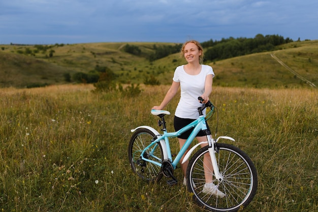 Mujer joven pelirroja con una bicicleta en el campo