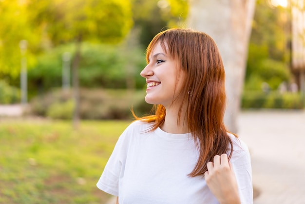 Mujer joven pelirroja bonita al aire libre con expresión feliz