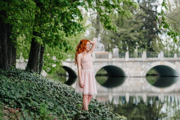 Mujer joven pelirroja caminando en un parque con gran mansión blanca