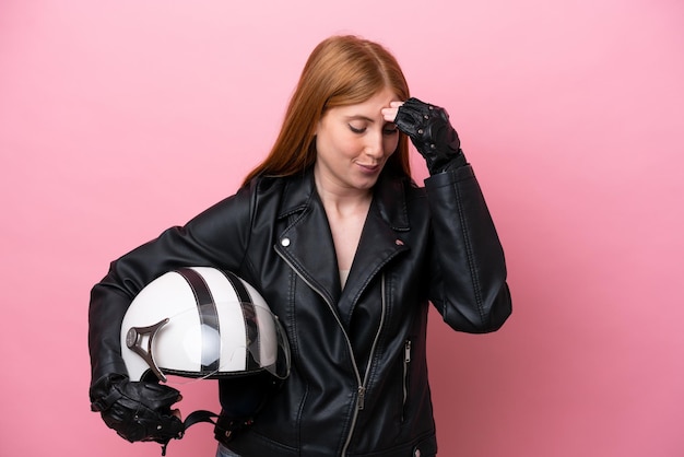 Mujer joven pelirroja con un casco de motocicleta aislado sobre fondo rosa riendo