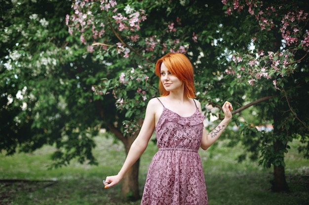 Mujer joven pelirroja cerca del árbol floreciente de la primavera, belleza natural