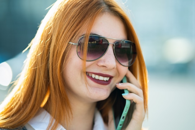 Mujer joven pelirroja con gafas de sol hablando por teléfono
