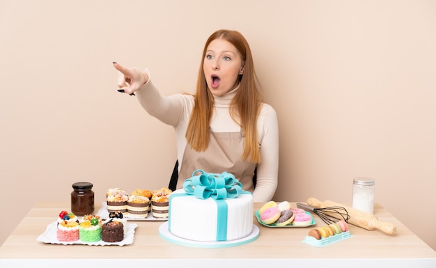 Foto mujer joven pelirroja con un gran pastel apuntando lejos