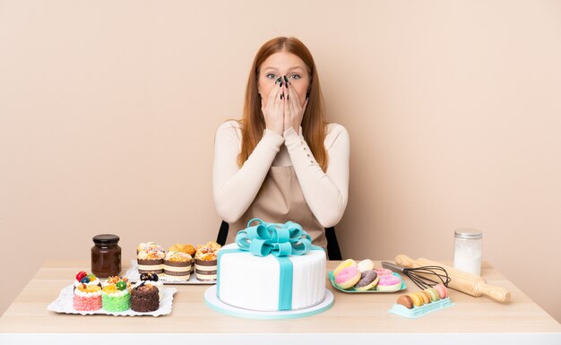 Mujer joven pelirroja con un gran pastel con expresión facial sorpresa