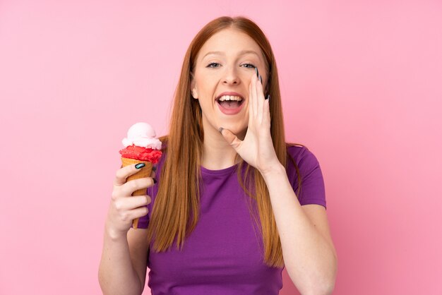 Mujer joven pelirroja con un helado de cucurucho gritando con la boca abierta