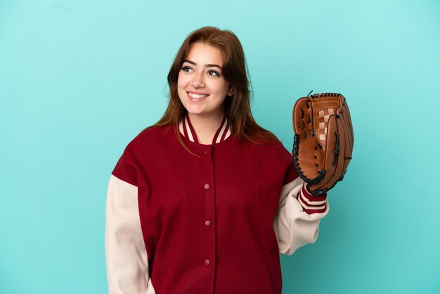 Mujer joven pelirroja jugando béisbol aislado sobre fondo azul pensando en una idea mientras mira hacia arriba