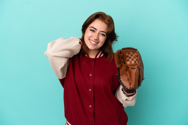 Mujer joven pelirroja jugando béisbol aislado sobre fondo azul riendo