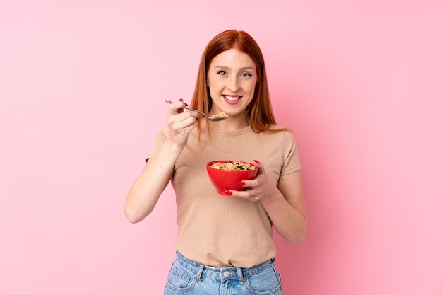 Mujer joven pelirroja sobre aislado sosteniendo un tazón de cereales